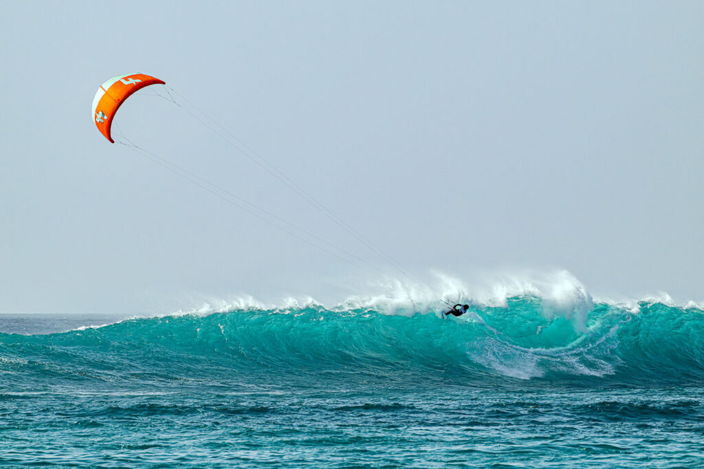 An orange kite above a kitesurfer on a wave