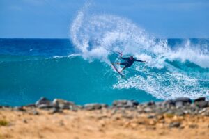 A kitesurfer carving a wave, with rocks in the foreground